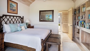 A bedroom with a large bed, wooden headboard, a ceiling fan, a bookshelf, and a door leading to another room. - Windermere Paradise: Luxurious Estate With Amenities (Governor's Harbour)