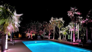 A swimming pool with lounge chairs and palm trees, surrounded by a well-lit patio area. - Windermere Paradise: Luxurious Estate With Amenities (Governor's Harbour)