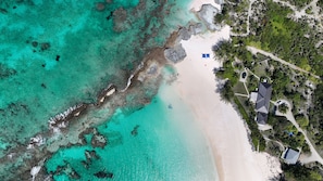 An aerial view of a beach resort with clear turquoise waters, a sandy beach, and a few buildings with a swimming pool. - Coastal Haven: Newly Renovated Beachfront Cottage With Pool (Governor's Harbour)