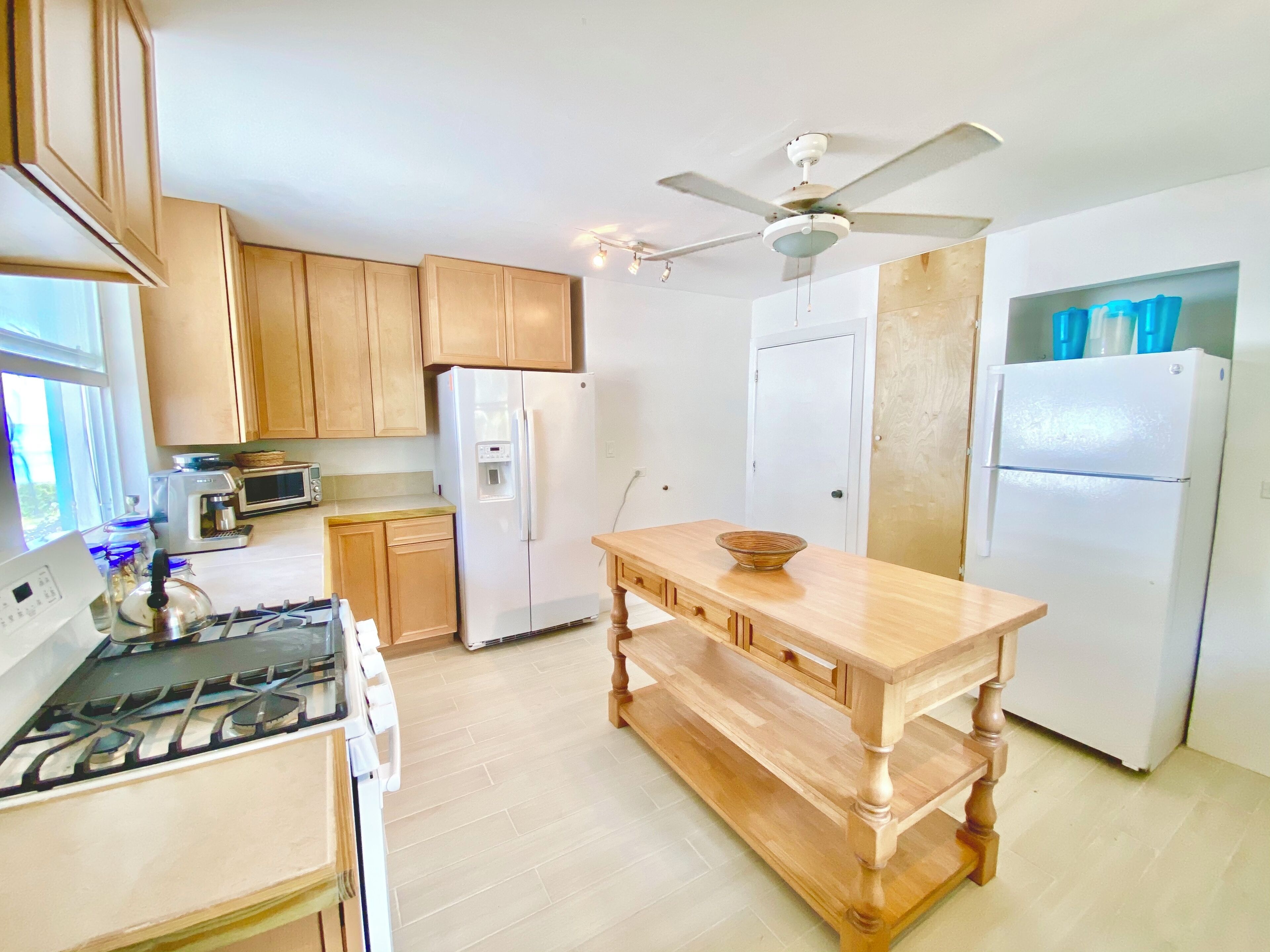 A kitchen with wooden cabinets, a white refrigerator, a microwave, a gas stove, and a ceiling fan.