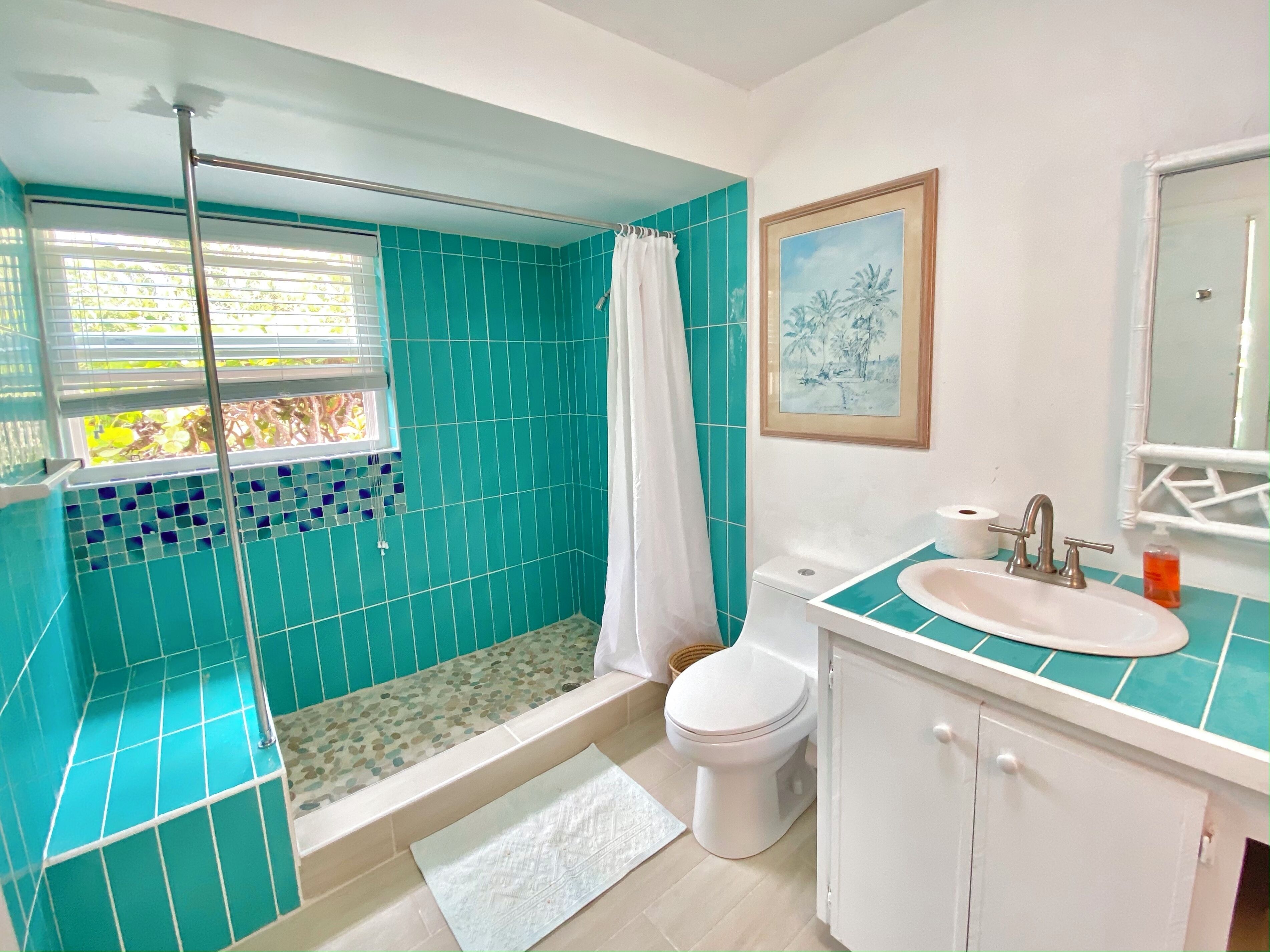 A bathroom with a shower, toilet, sink, and a window with a view of greenery.