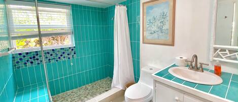 A bathroom with a shower, toilet, sink, and a window with a view of greenery.
