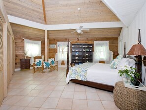 A spacious bedroom with a wooden ceiling, a large bed, a ceiling fan, and a built-in bookshelf. - Poponi Cottage Paradise: Pink Sand Retreat (North Palmetto Point)