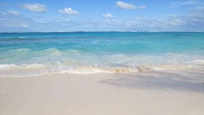 Una playa con agua turquesa cristalina y una orilla arenosa bajo un cielo azul con nubes dispersas.