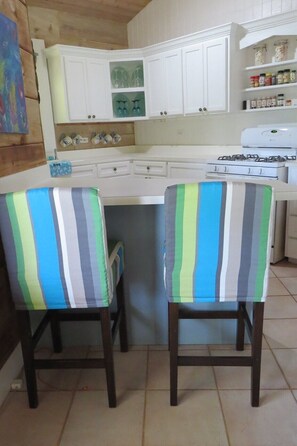 A kitchen with white cabinets, a stove, and two striped chairs. - Poponi Cottage Paradise: Pink Sand Retreat (North Palmetto Point)