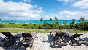 Four sun loungers facing a beach with turquoise water and palm trees. - Contemporary Comfort: Stunning Villa With Pool & Restaurant (Governor's Harbour)