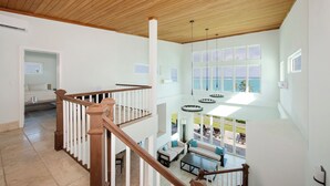 A spacious room with a high ceiling, a wooden staircase, and large windows overlooking a scenic view. - Contemporary Comfort: Stunning Villa With Pool & Restaurant (Governor's Harbour)