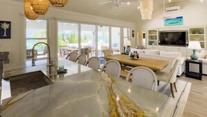 A spacious living area with a large island, dining chairs, a sofa, and a TV. - Pink Sand Paradise: Luxury Home With Heated Pool (North Palmetto Point)