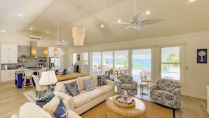 A spacious living area with a large sofa, two armchairs, a coffee table, and a dining table. There is a view of the ocean through large windows. - Pink Sand Paradise: Luxury Home With Heated Pool (North Palmetto Point)