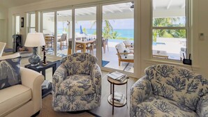 A spacious living room with a view of the ocean, featuring a sofa, two patterned armchairs, a coffee table, and a lamp. - Pink Sand Paradise: Luxury Home With Heated Pool (North Palmetto Point)