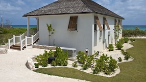 A white building with a sloped roof, a staircase leading to a porch, and a view of the ocean. - Coastal Chic: New Luxury Oceanfront Home With Sunset Views (Governor's Harbour)