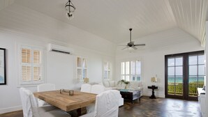 A spacious room with a wooden dining table, white upholstered chairs, a sofa, and a ceiling fan. - Coastal Chic: New Luxury Oceanfront Home With Sunset Views (Governor's Harbour)