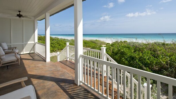 A covered porch with white railings, a ceiling fan, and a view of the ocean. - Coastal Chic: New Luxury Oceanfront Home With Sunset Views (Governor's Harbour)