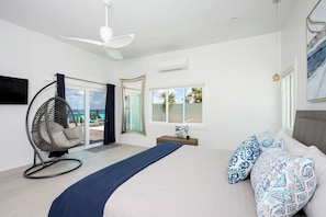 Un dormitorio con cama, una silla colgante, un ventanal con vistas y un ventilador de techo.