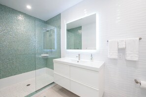 Un baño moderno con ducha envuelta en vidrio, tocador blanco y un espejo grande.