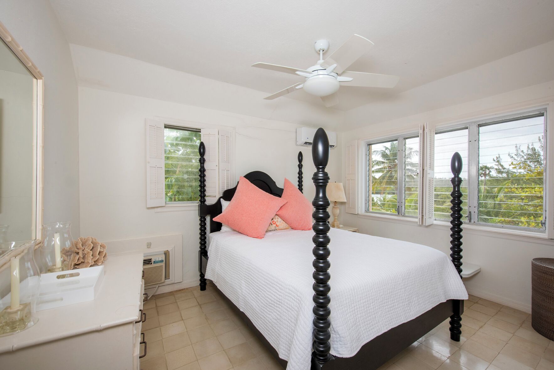 A bedroom with a four-poster bed, a ceiling fan, and windows with views of greenery.