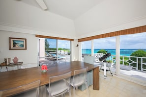 A spacious dining area with a wooden table and chairs, large windows with ocean views, and a telescope on the deck.