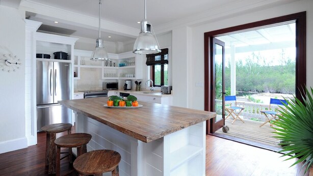 Een moderne keuken met een houten kookeiland, roestvrijstalen apparatuur en een groot raam met uitzicht op een terras.