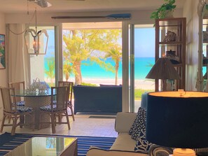 A room with a glass table, wicker chairs, a sofa, and a view of the beach. - Coastal Chic: Stylish Condo On Windermere Beach (Governor's Harbour)