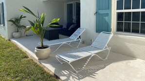 A balcony with two lounge chairs, a small table, and two potted plants. - Coastal Chic: Stylish Condo On Windermere Beach (Governor's Harbour)