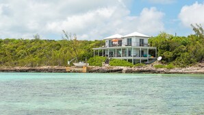 Une maison à deux étages dotée d’un balcon, située sur une côte rocheuse bordée d’une eau turquoise et cristalline.