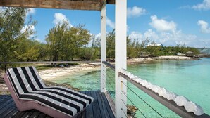 Une terrasse en bois avec un fauteuil de jardin à rayures et une vue sur une mer turquoise limpide et une plage de sable.