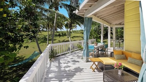 A wooden deck with a white railing, a yellow sofa, and a table with a vase of flowers. - Banks Road Beauty: Luxurious Beachfront Home (Governor's Harbour)