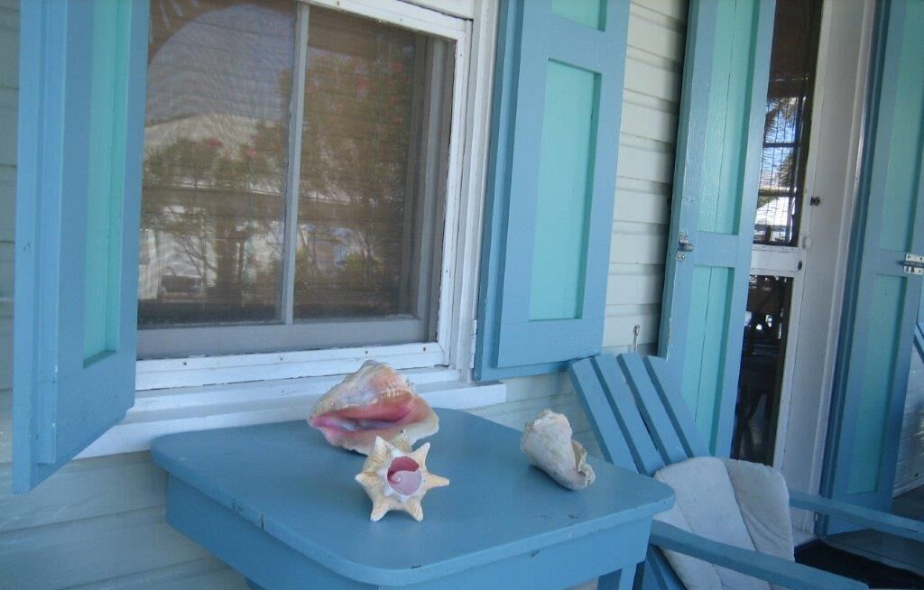 A porch with a blue table, two chairs, and a window with a view of trees.