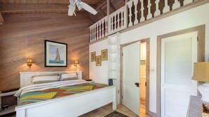 Un dormitorio con techo de madera, una cama con colcha de colores, dos lámparas de pared, un cuadro enmarcado y una puerta blanca.