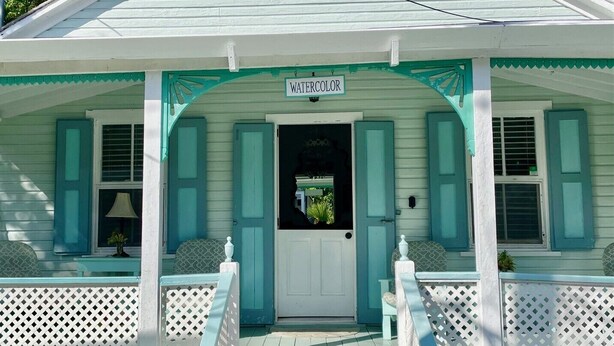 Una casa con porche, un letrero que dice 'WATERCOLOR' y una puerta con ventana.