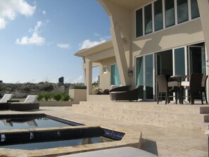 Un espace piscine extérieur moderne, doté de chaises longues et d’un coin repas.