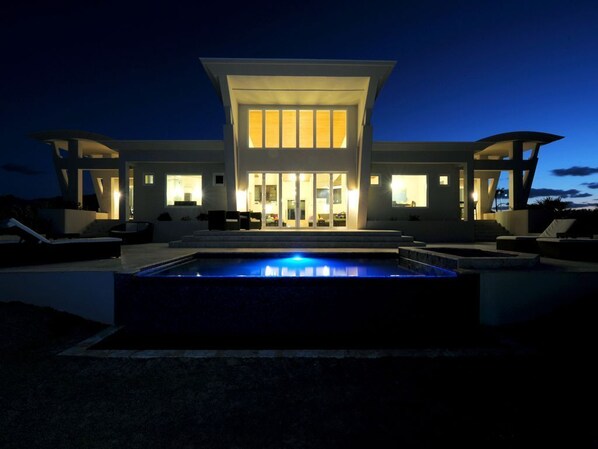 Une maison moderne dotée d’une piscine, de grandes fenêtres et d’un espace salon extérieur.