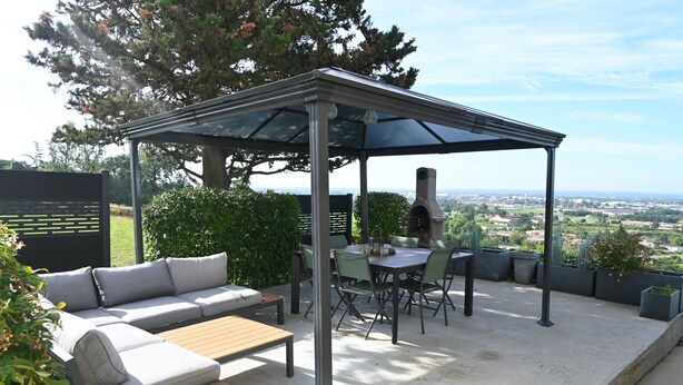 Een terras buiten met een overdekte zithoek, een tafel en stoelen.