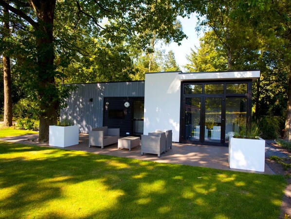 Un espacio exterior moderno con mobiliario integrado y puerta de cristal, rodeado de abundante vegetación.