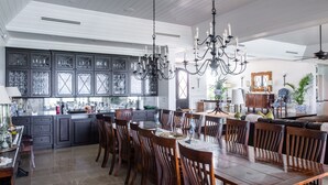 A spacious kitchen with dark cabinetry, a large dining table, and a chandelier. - Island Haven: Oceanfront Retreat With Infinity Pool (Blowing Point)