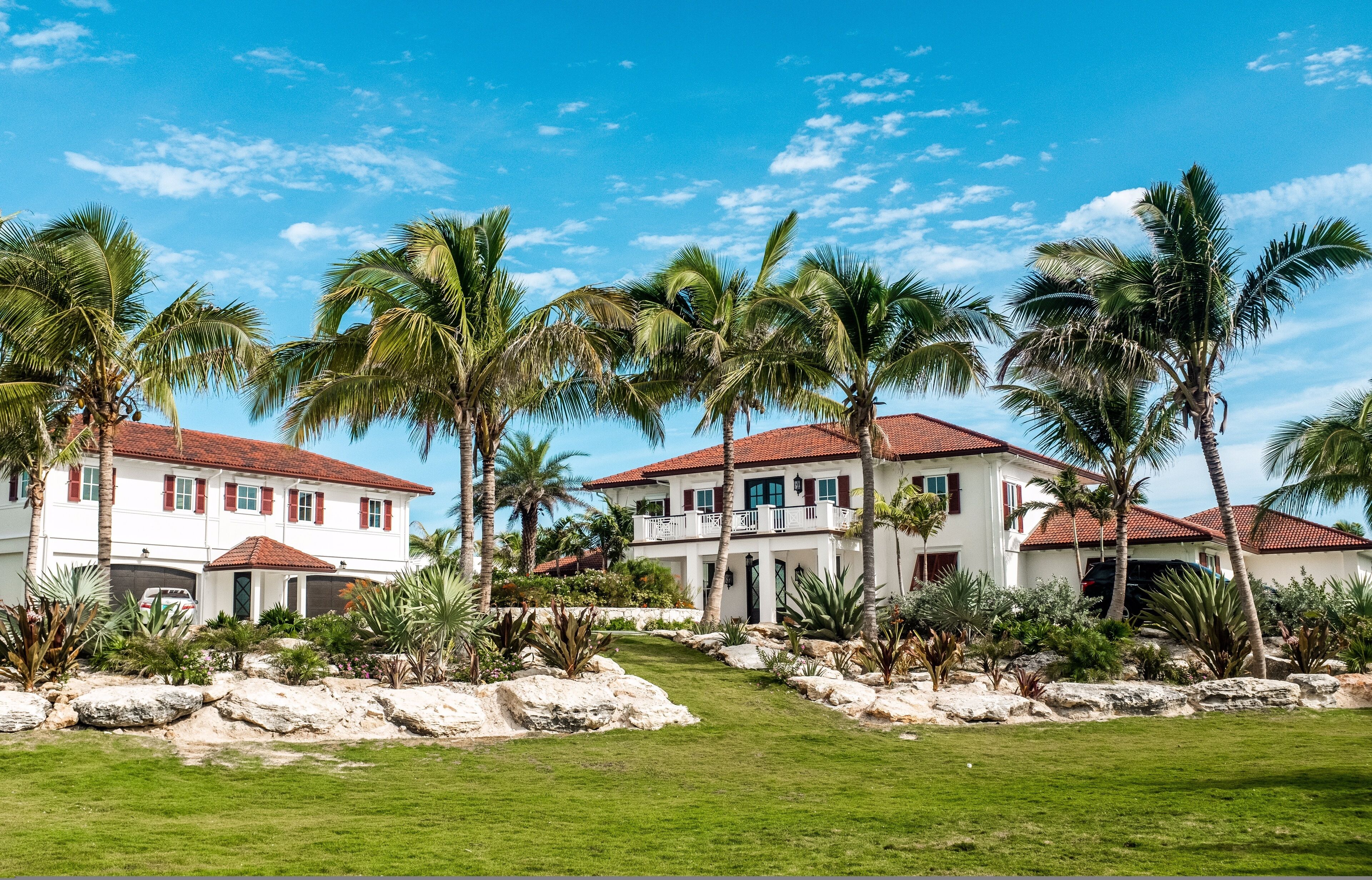A two-story house with a red-tiled roof, surrounded by palm trees and a well-maintained lawn.