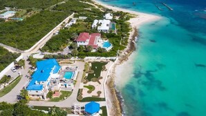 An aerial view of a coastal resort with multiple buildings, a beach, and clear turquoise waters. - Beachfront Bliss: Private Retreat With Spectacular Views (Blowing Point)