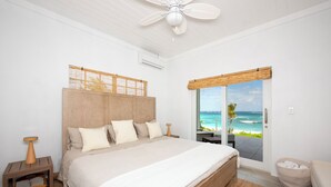 Une chambre avec un grand lit, un ventilateur de plafond, une vue sur l’océan et un panier en osier.