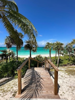 Een houten trap die naar een strand leidt, met turquoise water en palmbomen.