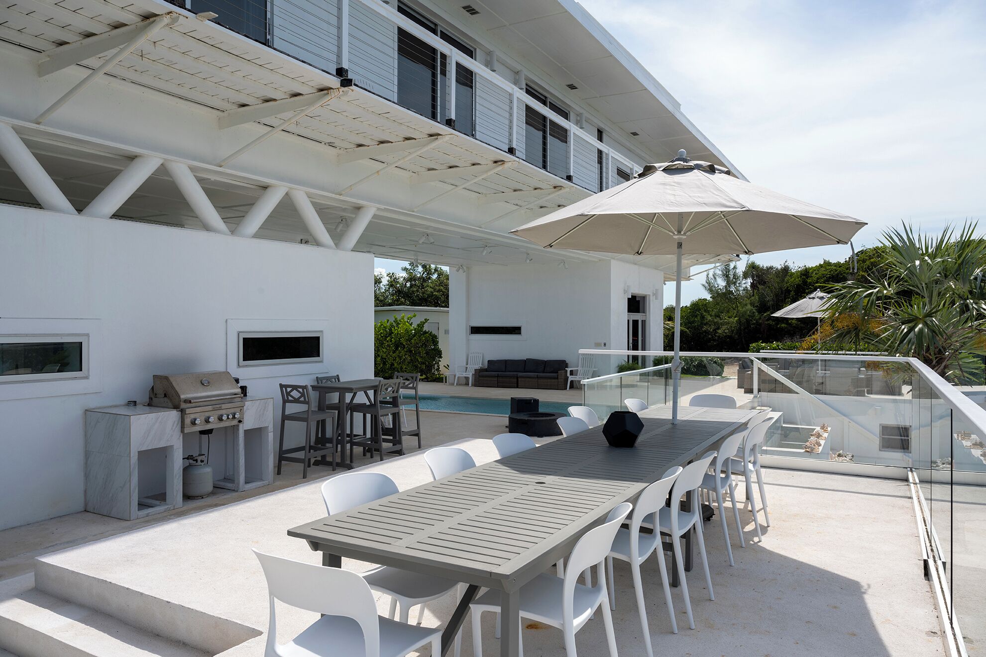 Une terrasse extérieure avec une piscine, un barbecue et un espace repas comprenant des chaises et une table.