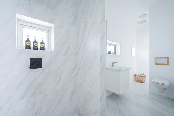 A modern bathroom with a marble floor, a white sink, a toilet, and a window with bottles of BYPRO soap.