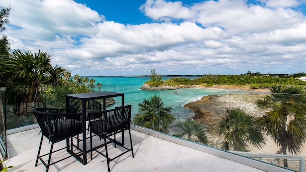 Ein Balkon mit Tisch und Stühlen mit Blick auf einen Strand und türkisblaues Wasser.