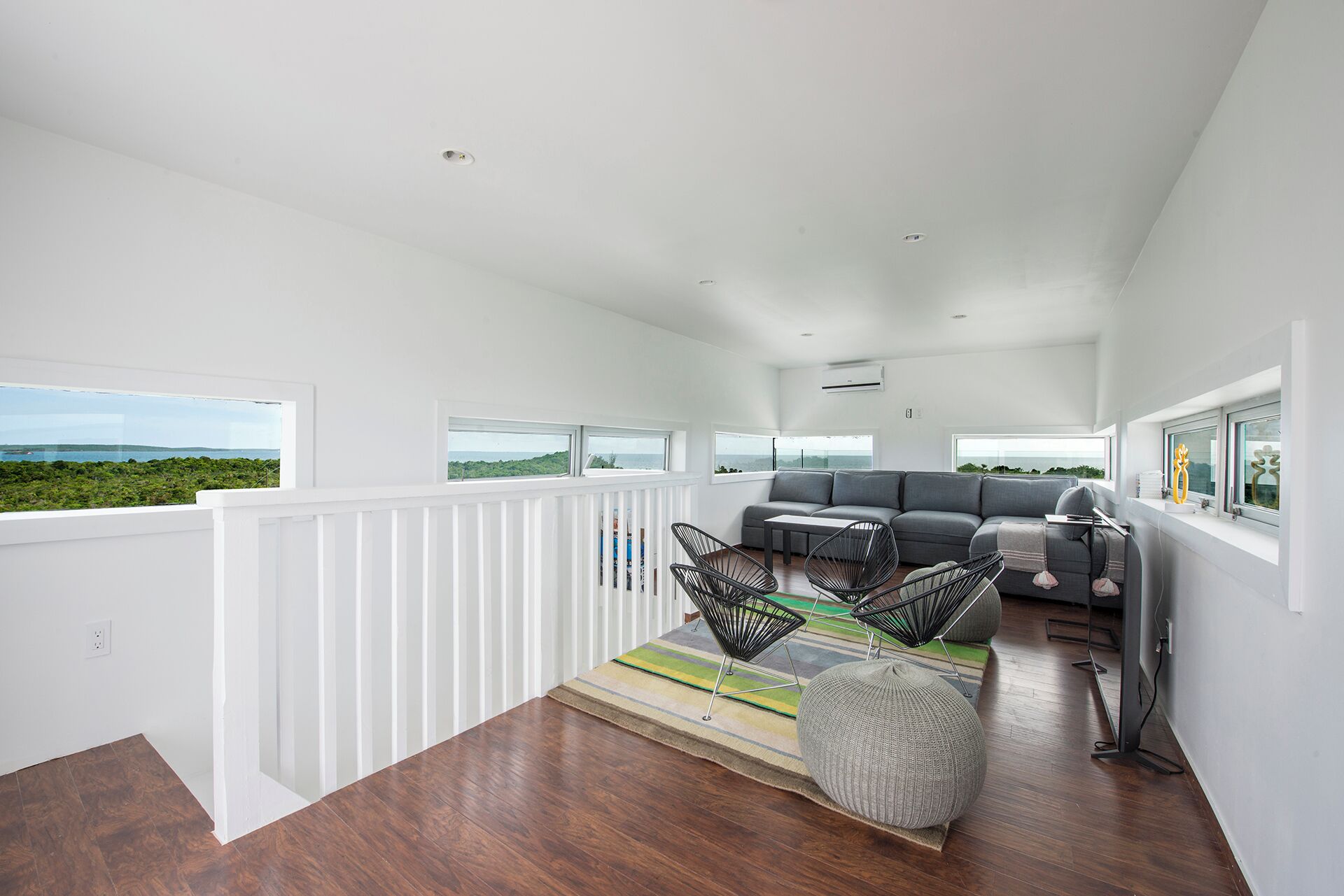 Ein geräumiger Balkon mit Meerblick, ein graues Sofa, schwarze Gestellstühle und ein kleiner Tisch.