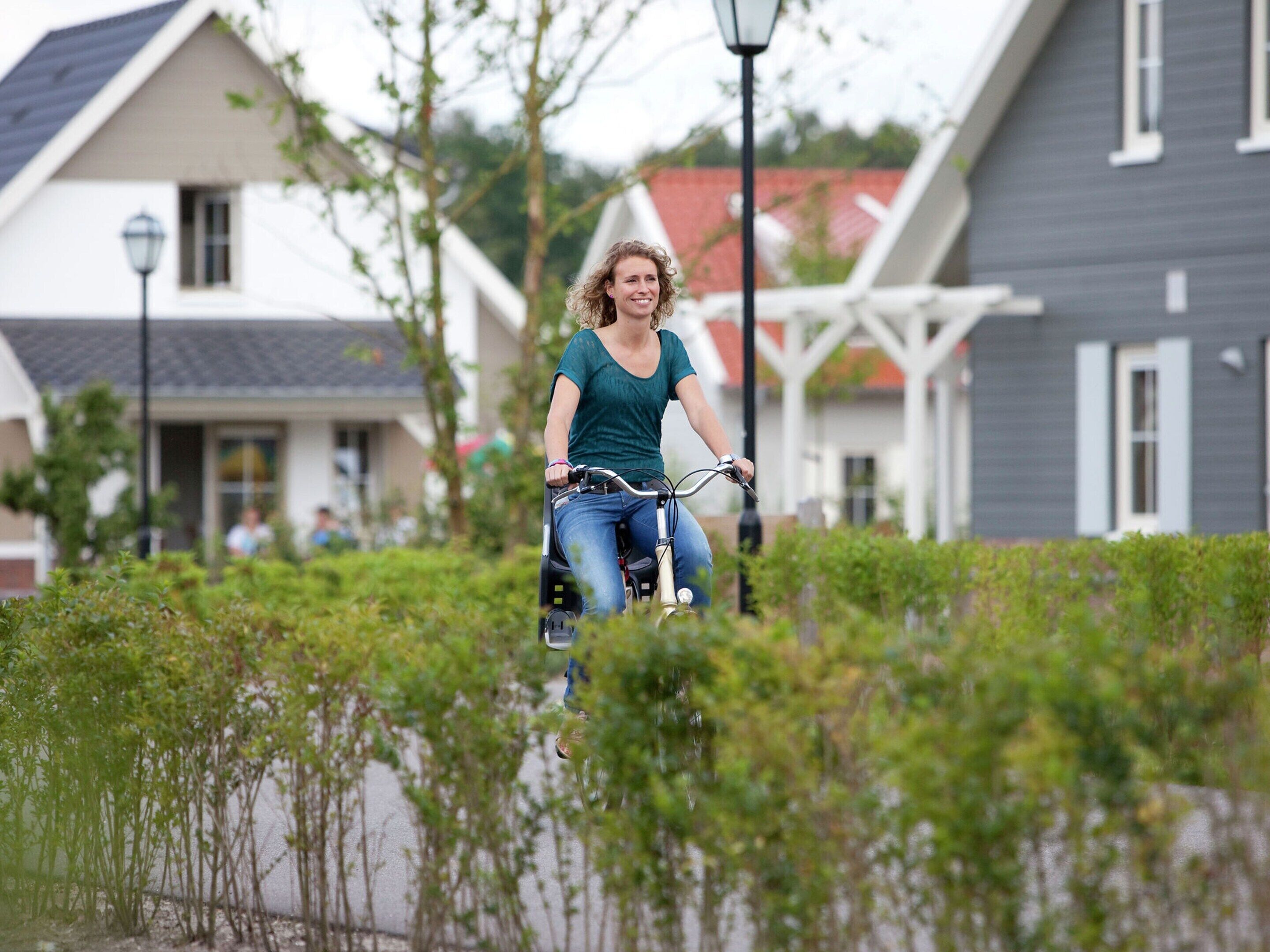 En person cykler på en sti med grøn bevoksning og huse i baggrunden.