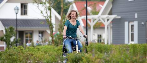En person cykler på en sti med grøn bevoksning og huse i baggrunden.