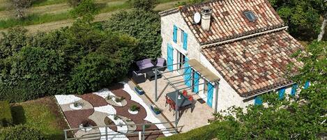 Une maison avec un toit en tuiles, une terrasse avec des sièges et un jardin.