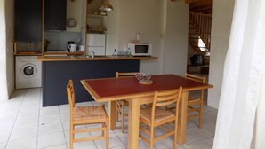 Cozinha compacta com vigas de madeira, ilha central e área de jantar com mesa vermelha e cadeiras de madeira.