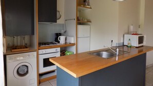 Uma cozinha compacta com máquina de lavar, forno, micro-ondas e bancada de madeira.