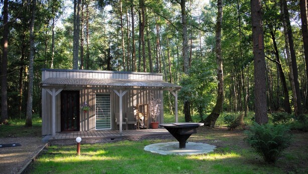 A wooden cabin with a porch, surrounded by a forest. - Asmonai Campsite (Kintai)
