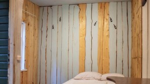 A small, cozy room with a single bed, a wooden wall with vertical planks, a small window, and a round table.
